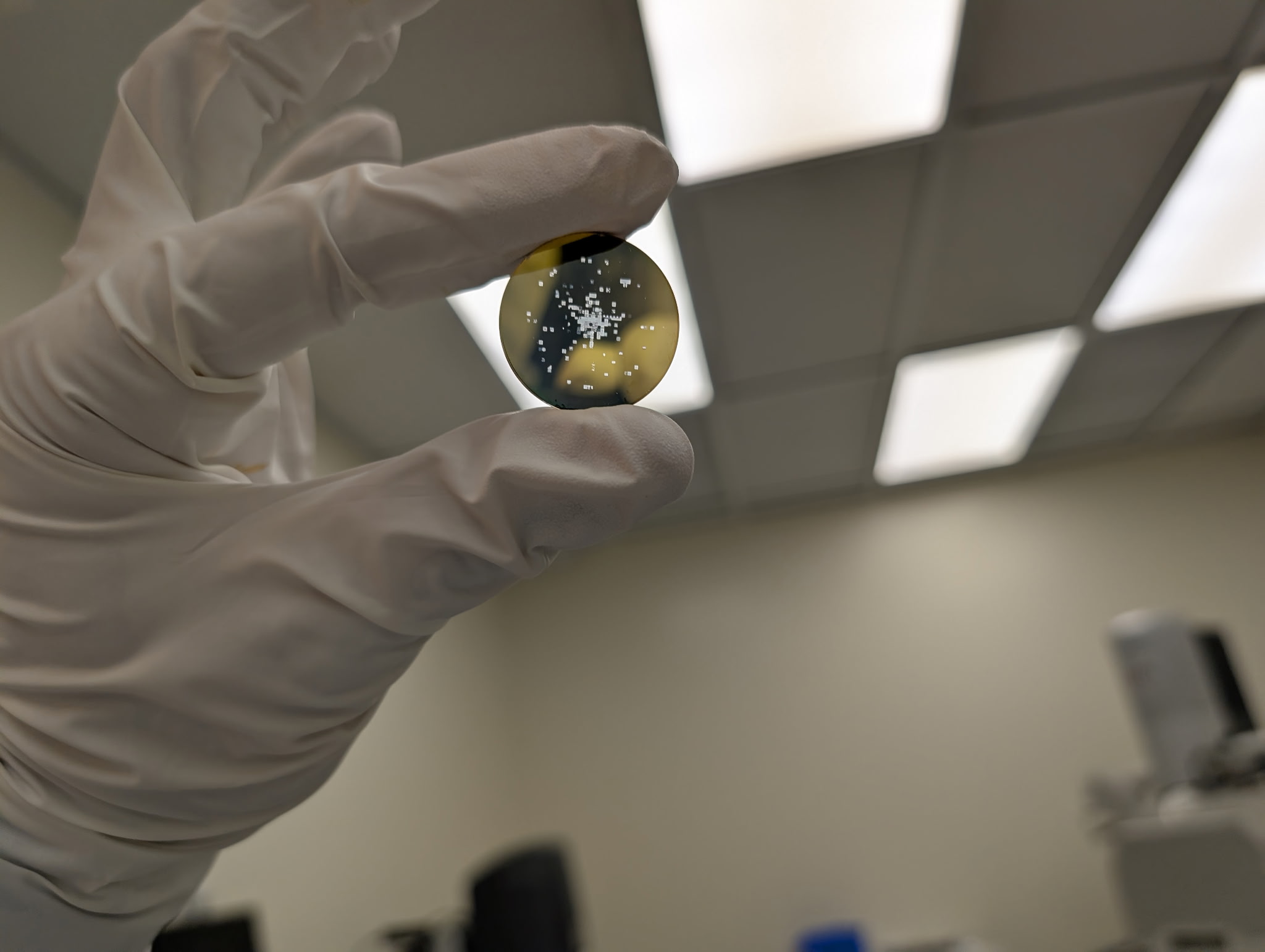 The Mosaic disk &mdash; a 29mm sapphire wafer with gold-etched contents, held in a gloved hand